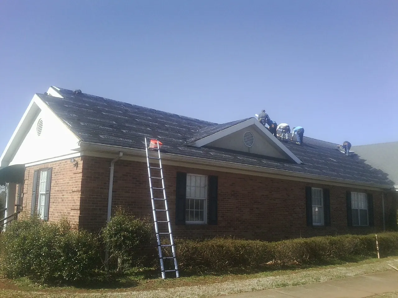 Crew tearing shingles off a brick ranch roof with a ladder set — Emergency Roof Repair work by our crew in White City