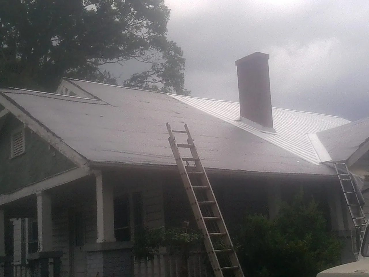 Ladders against a metal roof on an older home with a brick chimney in White City