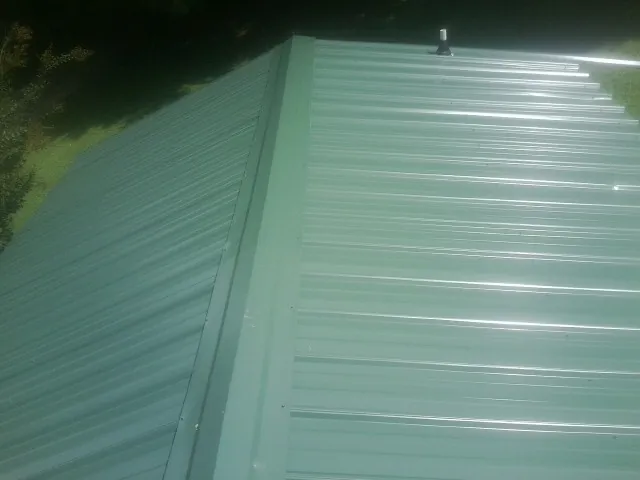New green metal panels meeting at the ridge of a roof — Flat Roof Repair work by our crew in White City